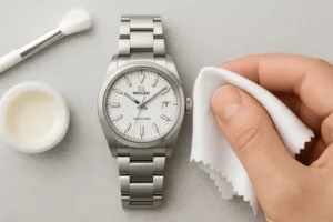 Mano-che-tiene-panno-microfibra-per-pulire-orologio-Nucleo-Date-quadrante-bianco-cassa-e-bracciale-acciaio-sulla-sinistra-barattolino-con-lucidante-e-pennello
